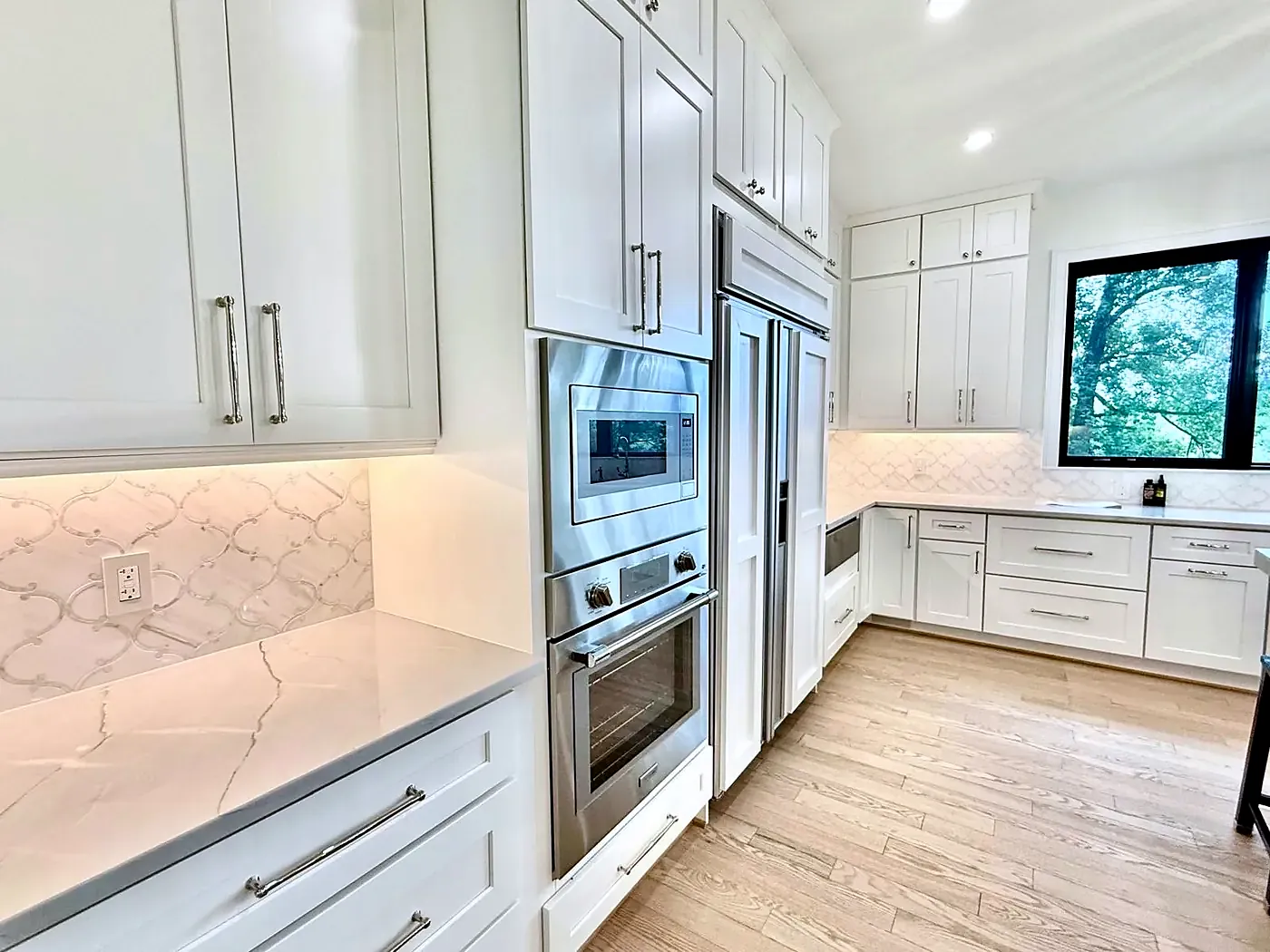 White shaker cabinets with a stainless wall oven, microwave and marble-pattern backsplash