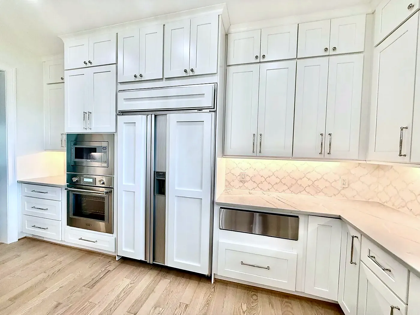 Kitchen wall with a paneled built-in refrigerator, wall oven, white cabinets and light wood floor