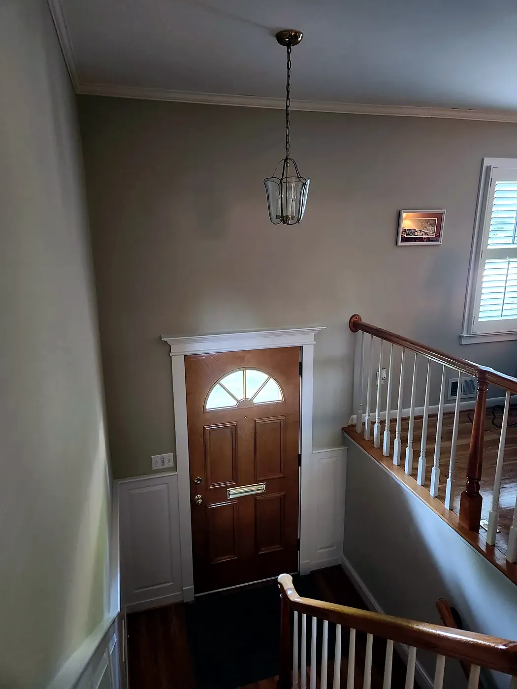 Small glass lantern pendant hanging in a foyer above a wood front door with fan window and stair railing