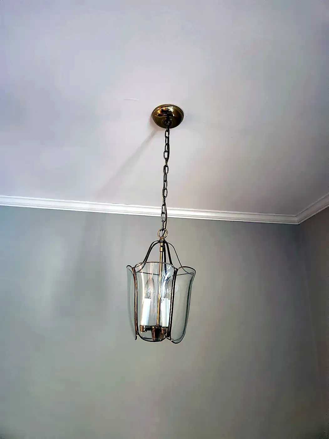 Brass lantern pendant with clear glass panels hanging on a chain from a white ceiling