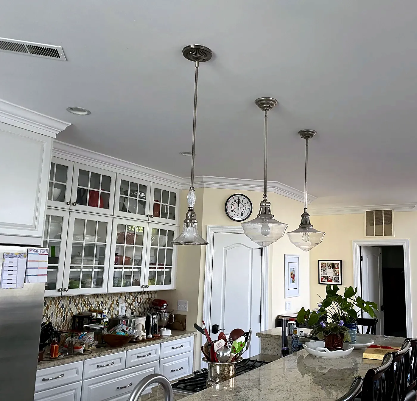 Three glass pendant lights over a granite kitchen island with white cabinets and a wall clock behind