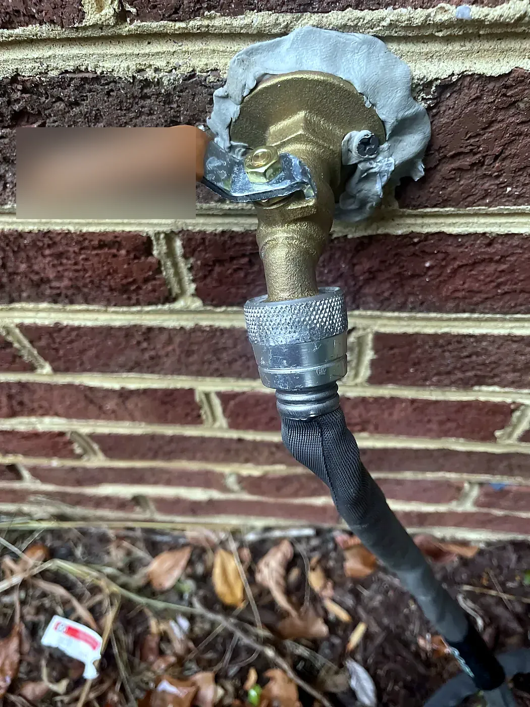 New brass quarter-turn hose bib with an orange handle on a red brick wall, hose attached