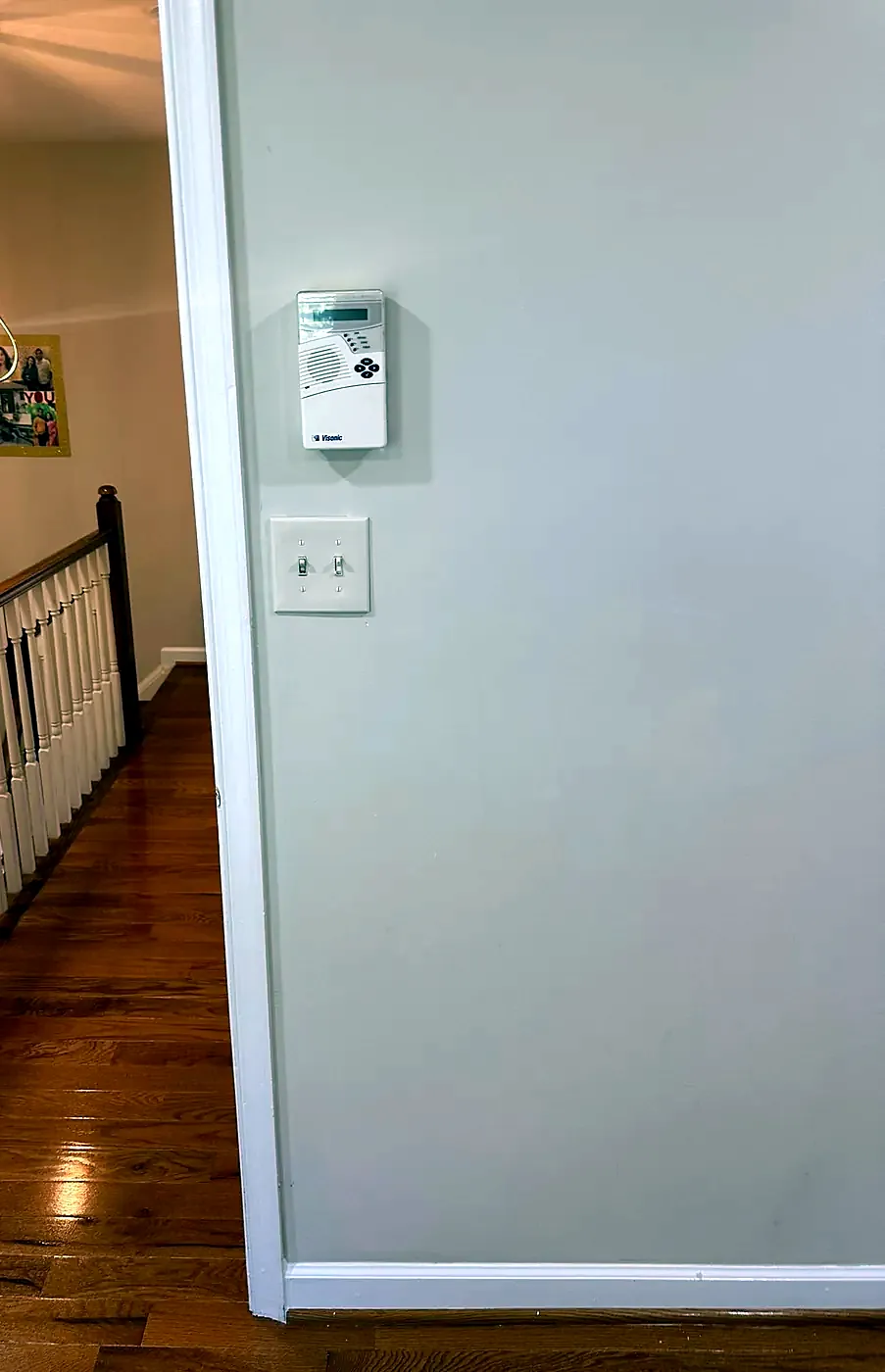 Hallway wall with a switch plate and thermostat near a stair railing and pendant light