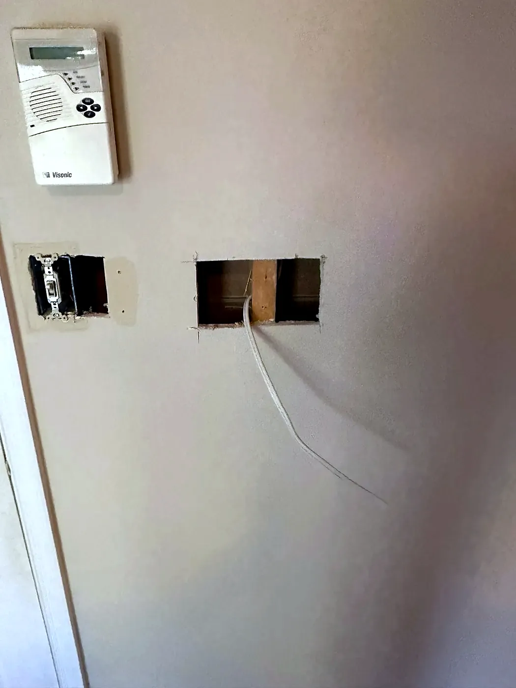 Two rough holes cut in a painted wall with wires showing, below an old thermostat
