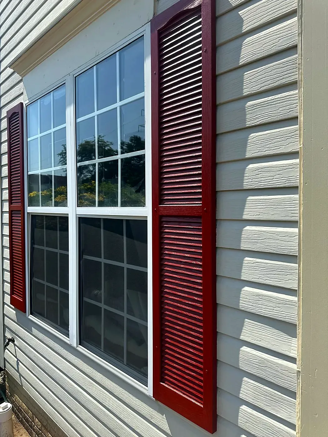 Deep red louvered shutters flanking a white-trimmed window on gray horizontal siding, close up