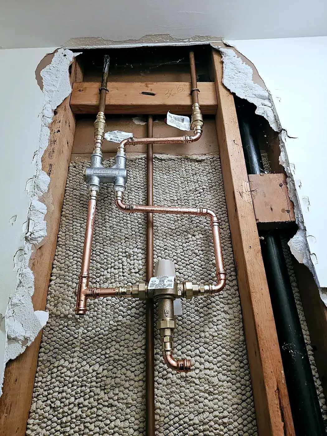 Cut-open plaster wall showing new copper pipes and brass valves against wire lath between wood studs