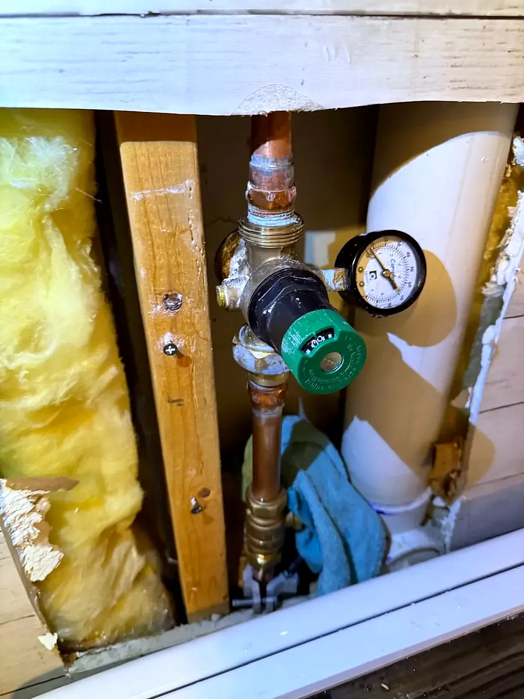 Pressure reducing valve and gauge on copper pipe inside an open wall with yellow insulation