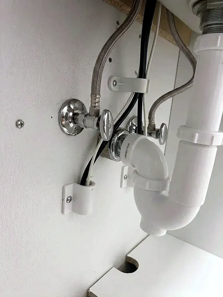 Two chrome shut-off valves with braided supply lines and a white P-trap under a bathroom sink