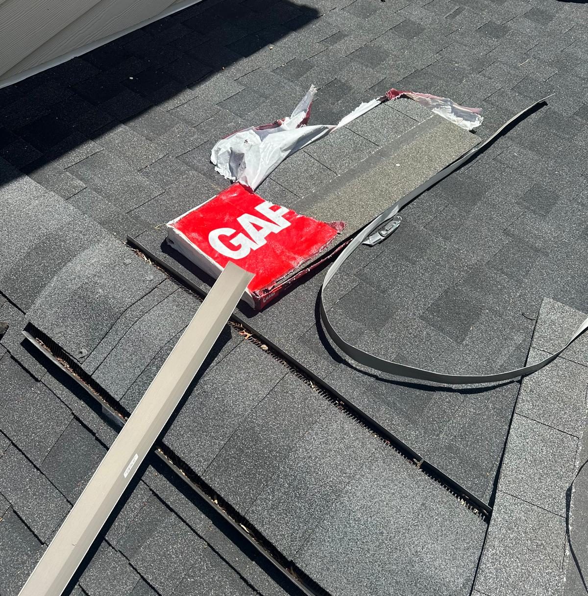 Old flashing removed from a roof-to-wall joint with new flashing stock laid out on the shingles