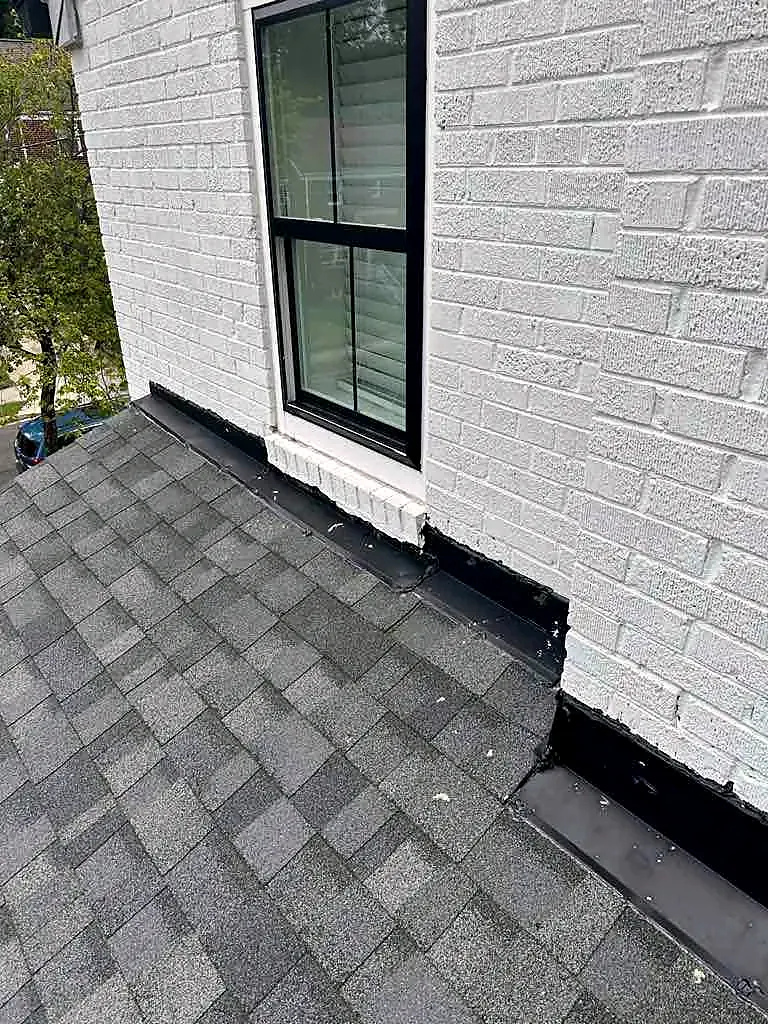 Gray shingle roof meeting a white painted brick wall with a black-framed window above