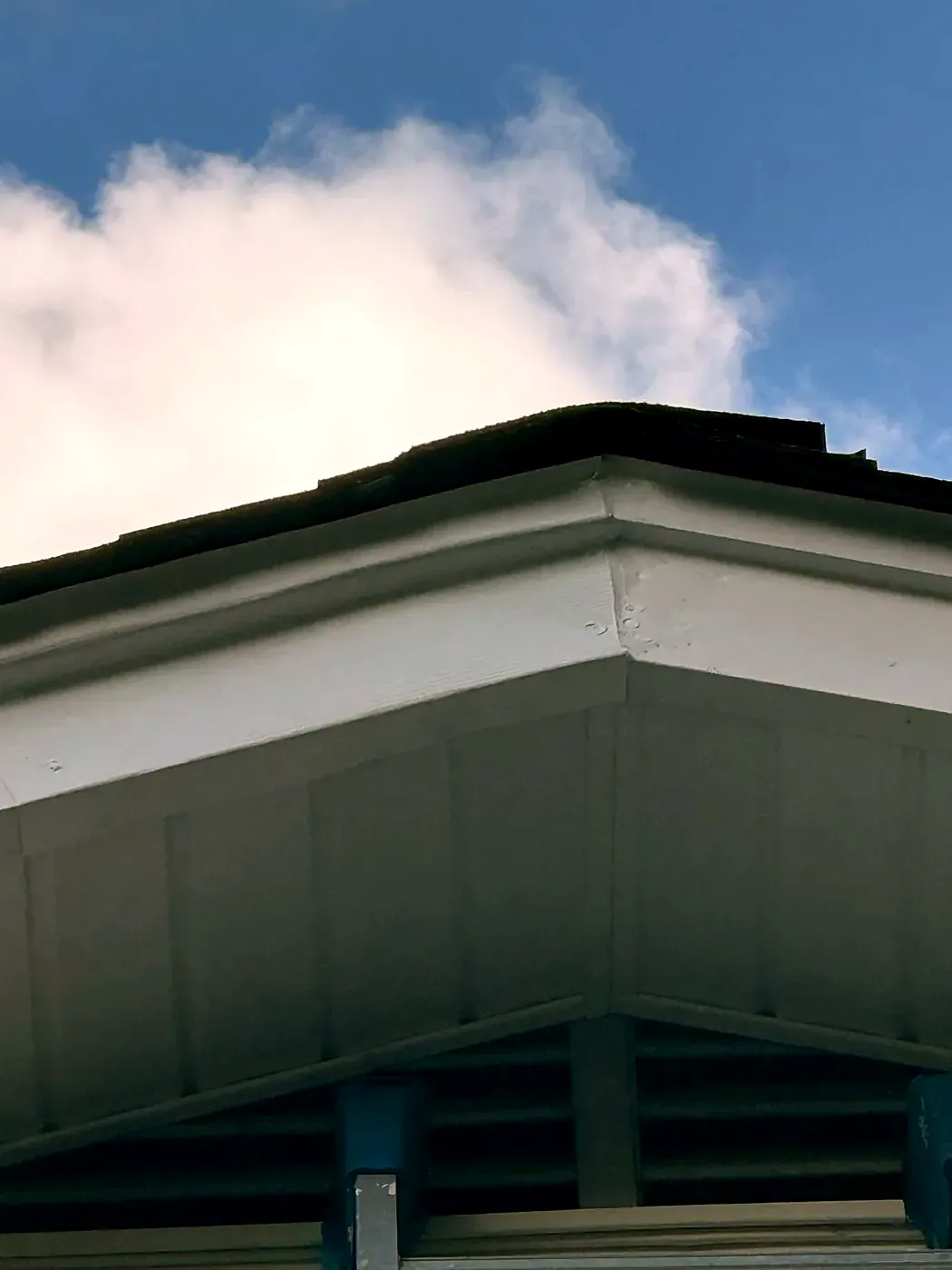 Repaired white fascia and gray soffit at a roof corner against a blue sky with clouds