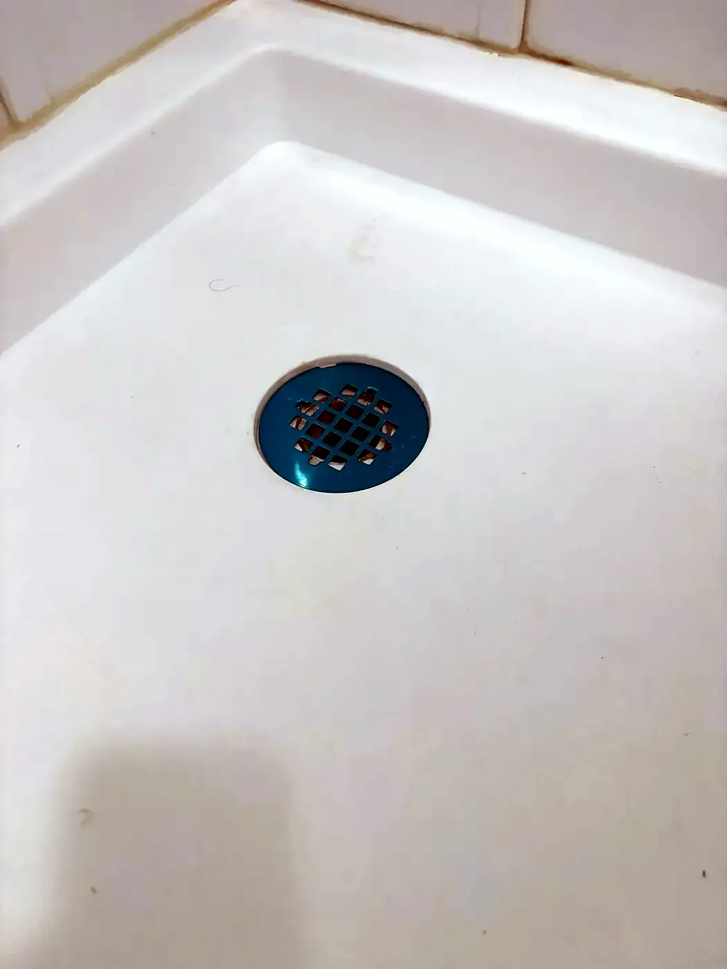 White shower pan with a new round drain strainer set flush in the center