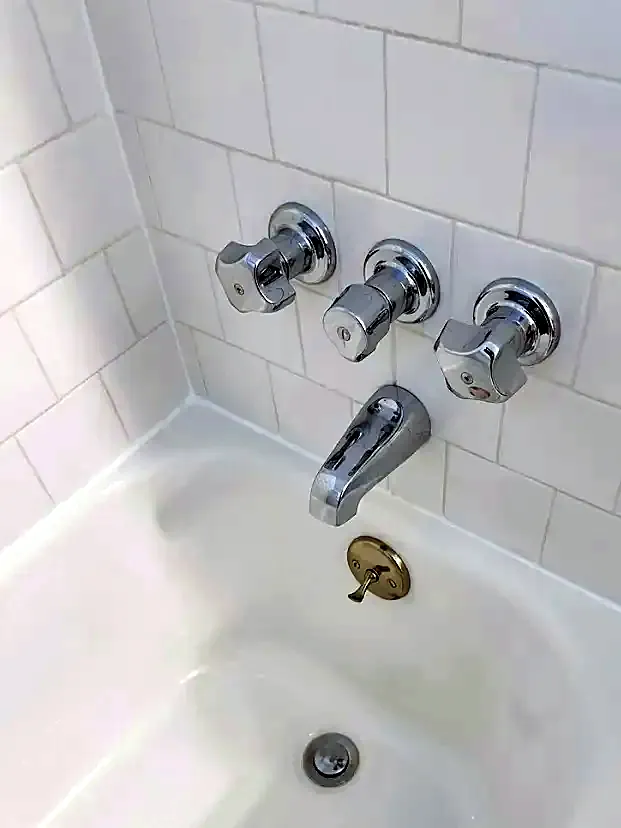 Three chrome handles and a chrome spout on white tile over a white bathtub