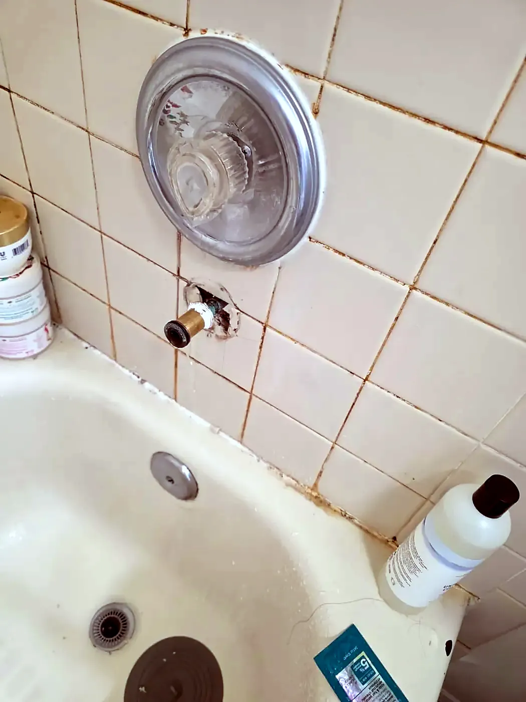 Old single-handle tub valve with corroded trim and rust-stained grout on white tile