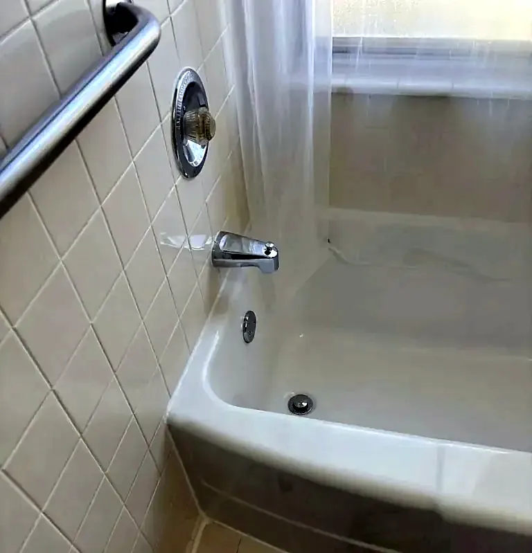 Chrome single-handle valve and tub spout on white tile with a stainless grab bar above