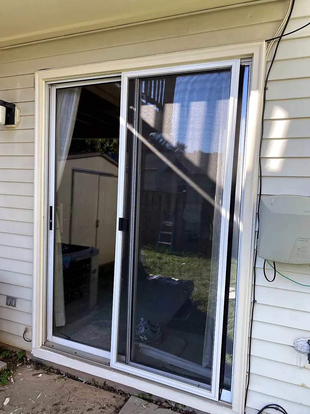 White-framed sliding patio door in cream siding, backyard visible through the glass