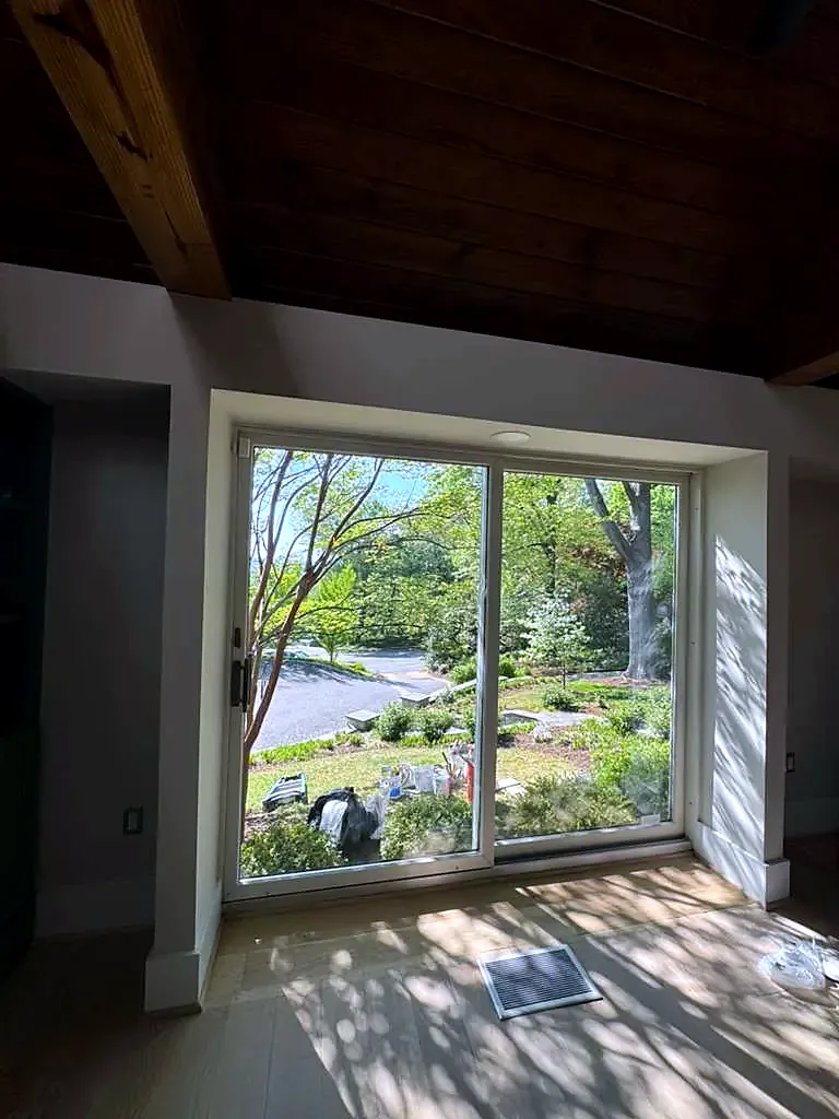 Sliding glass door viewed from inside a room with a wood ceiling, garden and trees outside