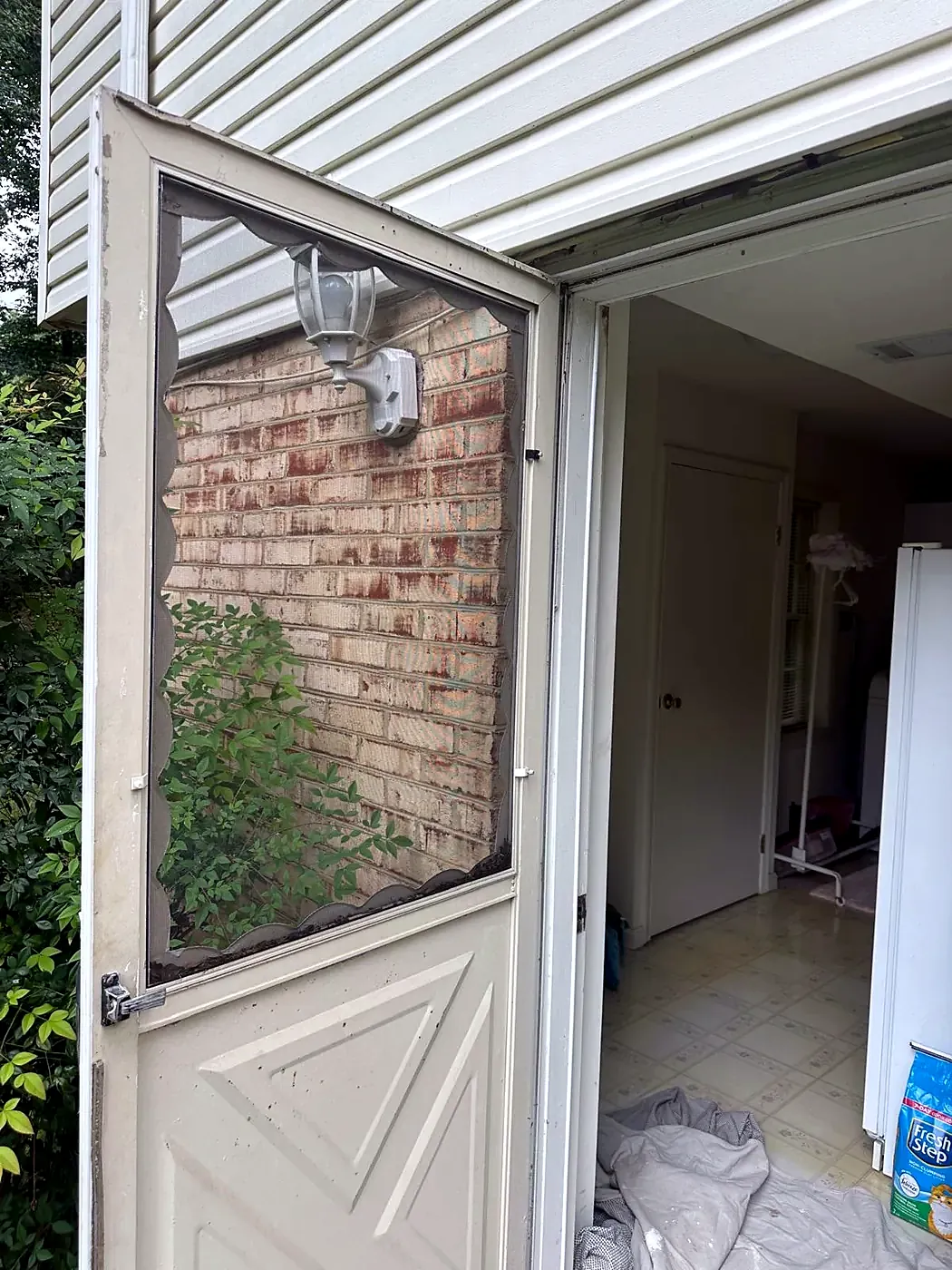 Cream half-glass storm door standing open at a side entry with brick wall and white siding