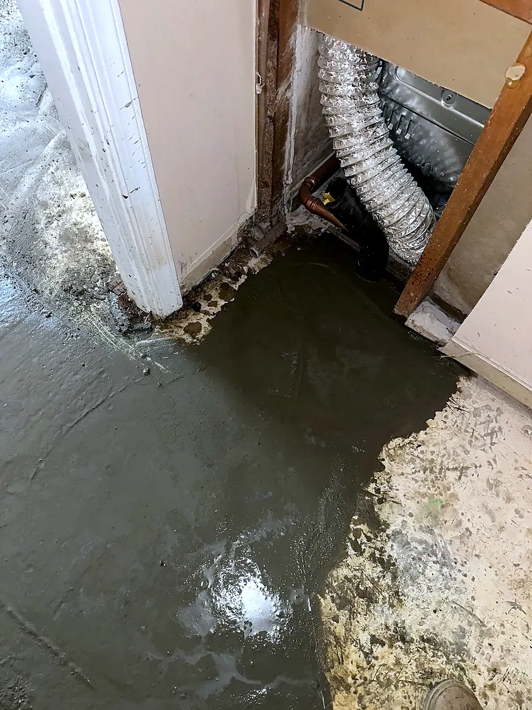 Wet basement floor with standing water at a door frame and a flex duct visible above