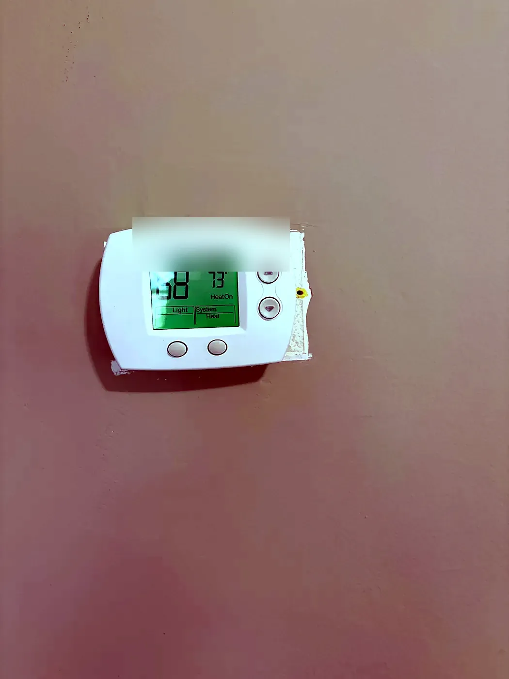 White thermostat with lit green display mounted on a plain beige wall