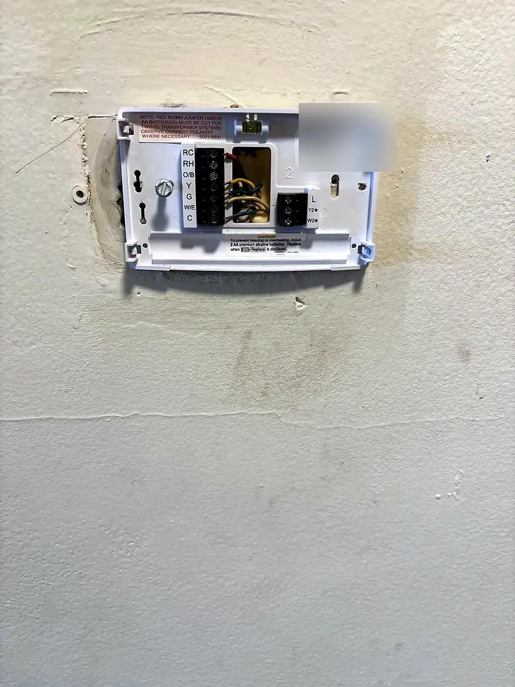 Thermostat base plate with exposed wire terminals mounted on a patched wall, cover removed