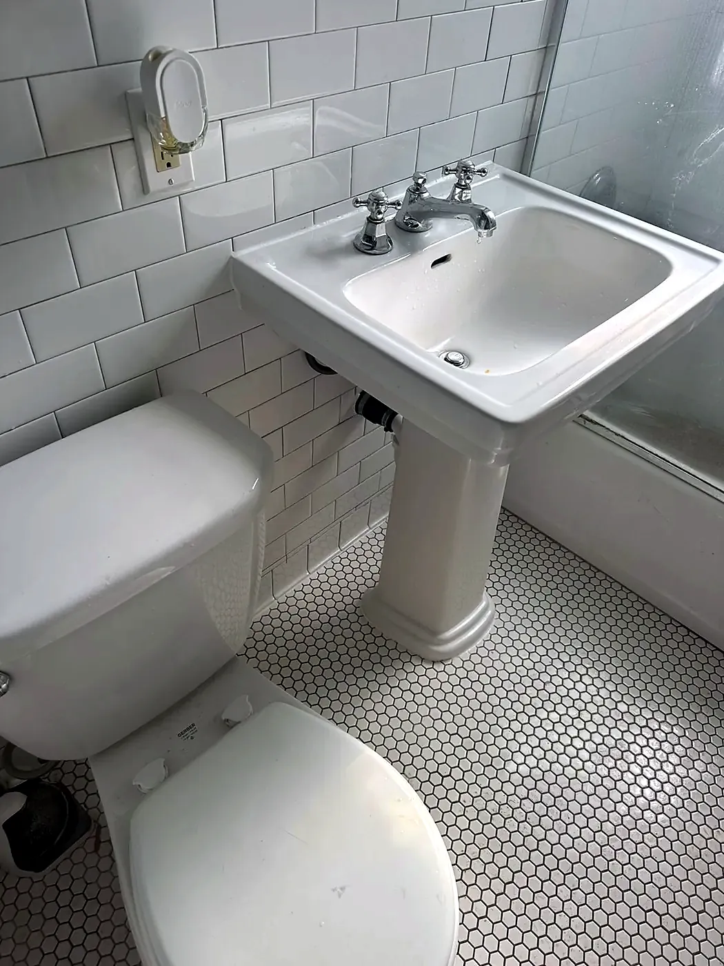 White penny tile bathroom floor with a pedestal sink and toilet, white subway tile walls