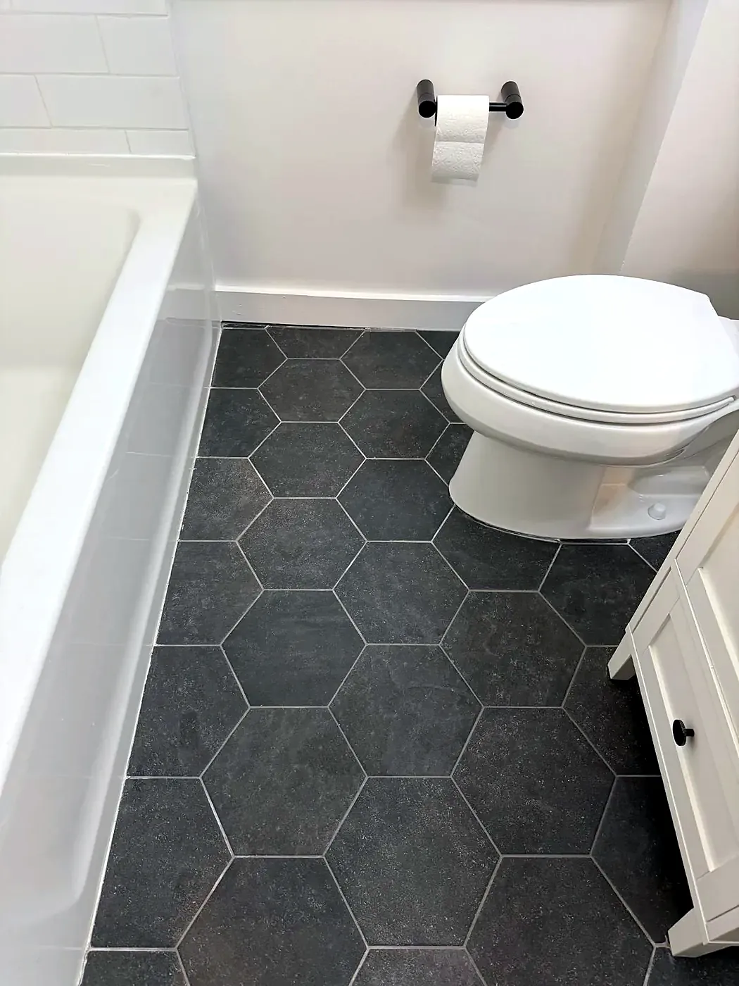 Clean dark hexagon tile bathroom floor with a white toilet and tub