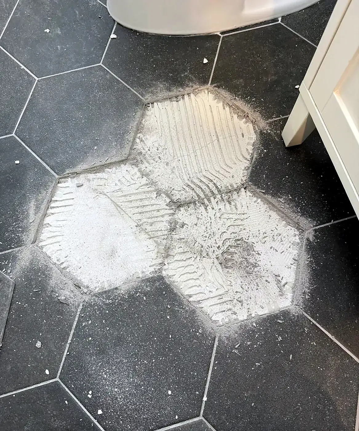 Dark gray hexagon tile floor with three tiles removed and the thinset bed exposed