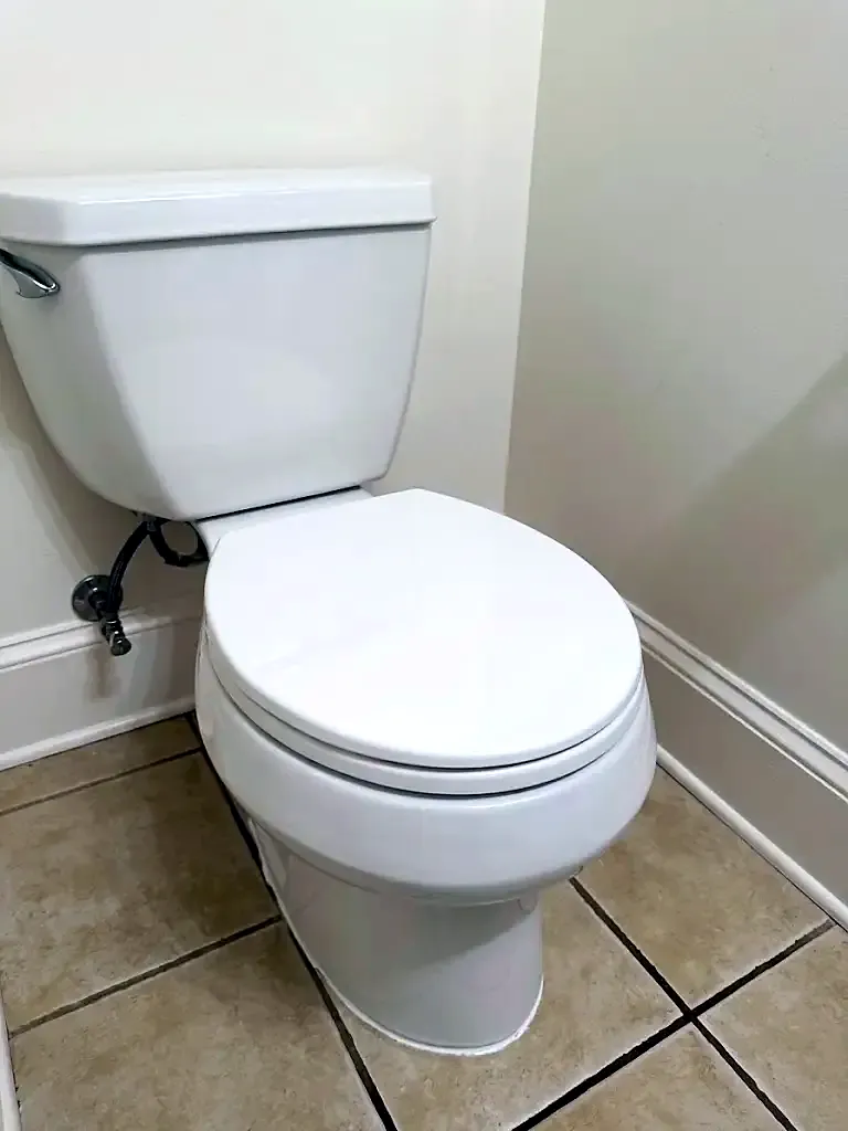 New white toilet on a beige tile floor in a corner with the supply line connected
