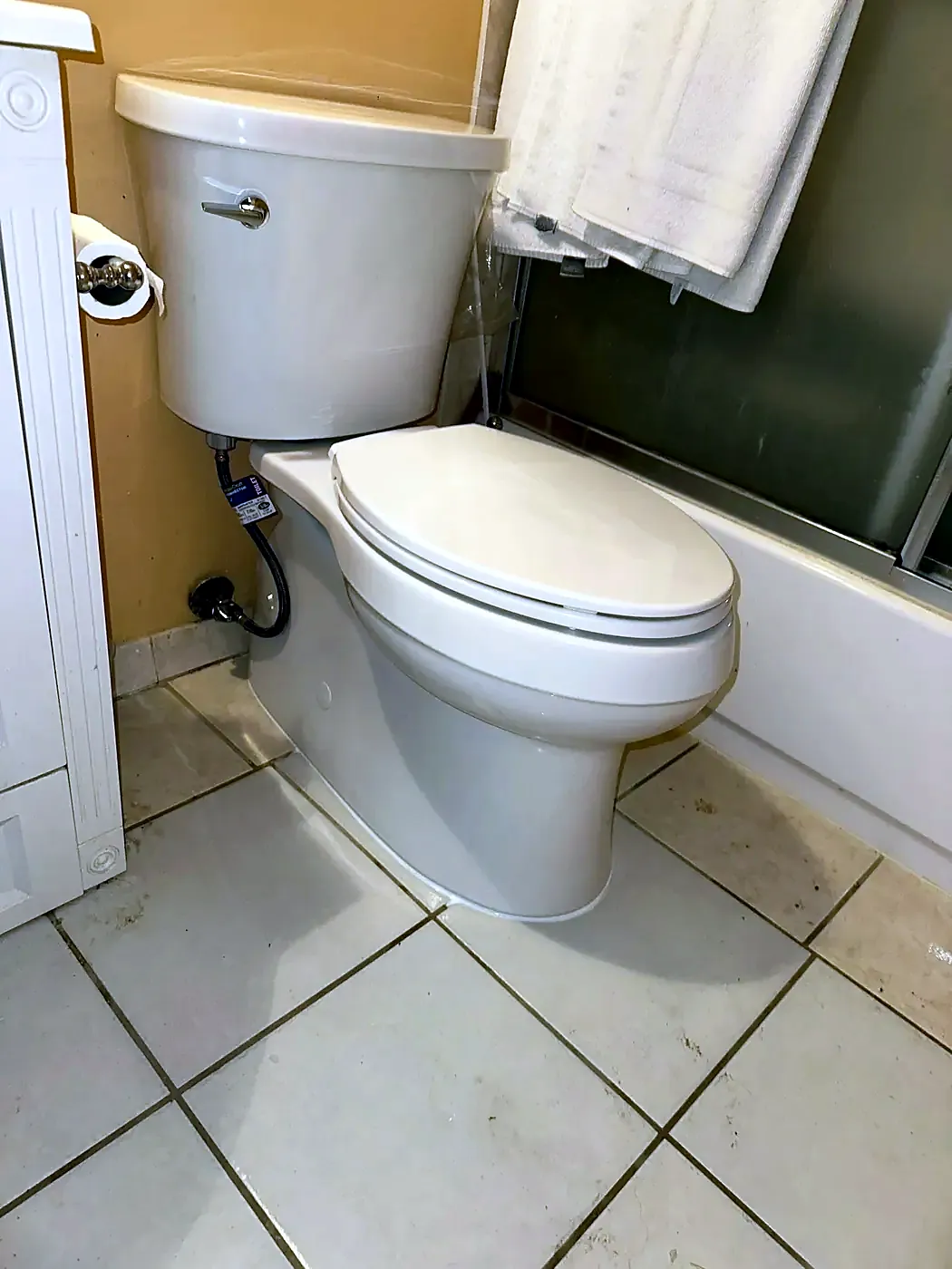 White toilet on tile beside a bathtub with a chrome supply line and valve at the wall