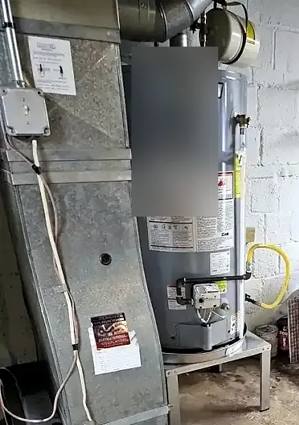 Gray gas water heater on a stand next to a furnace in a basement with block walls and overhead piping