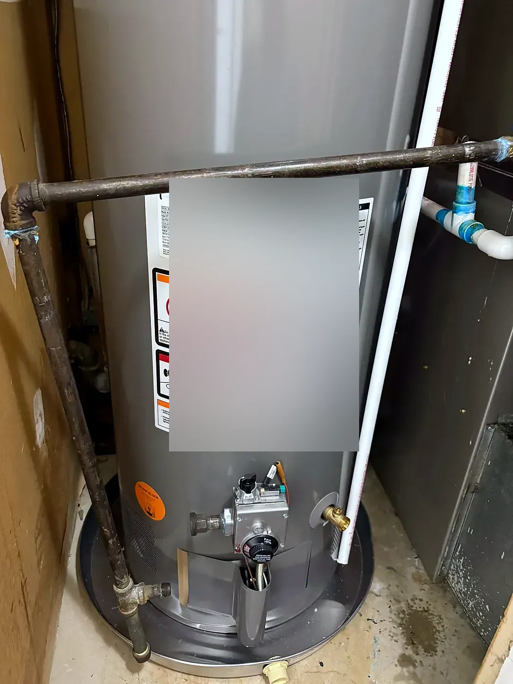 Front of a gray gas water heater showing the control valve, warning labels and black gas pipe