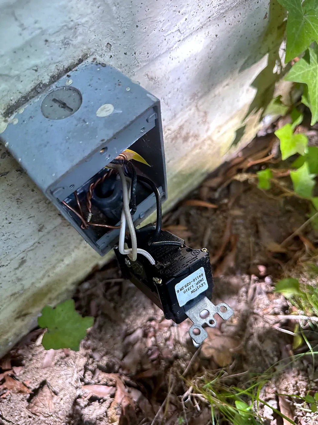 Open gray metal junction box on a foundation wall with wires and a small transformer hanging out
