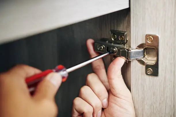 technician adjusting a cabinet door hinge with a screwdriver during professional hinge repair service.
