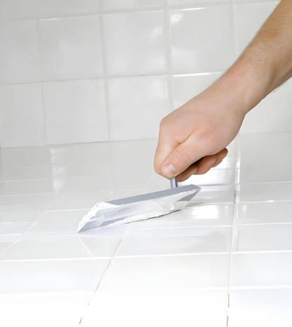 bathroom tile regrout in herndon va showing a pro spreading fresh grout over a clean white tile floor.