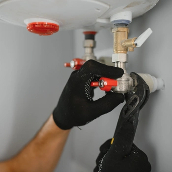 a professional technician wearing protective black grip gloves uses a specialized wrench to adjust a brass valve and pressure fittings during a comprehensive boiler repair in fairfax station va.