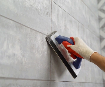 gloved hand smoothing fresh caulk along tiled wall joints during professional caulking service.