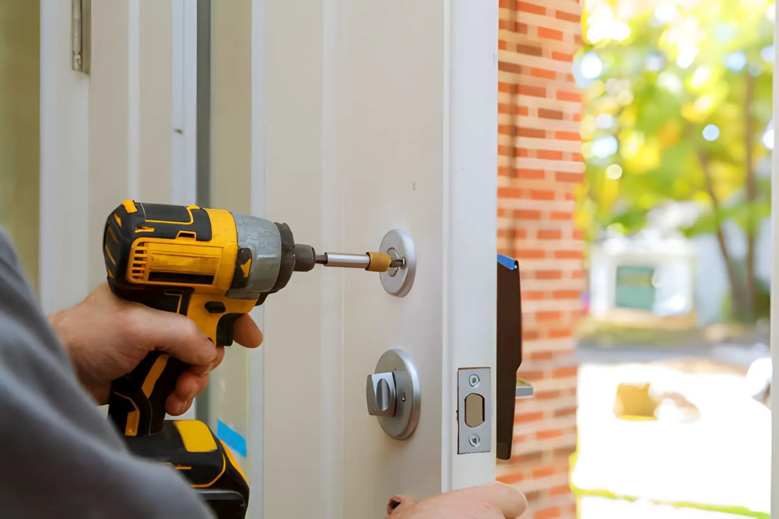 technician using a power drill to install a door lock and handle during a residential door installation service.