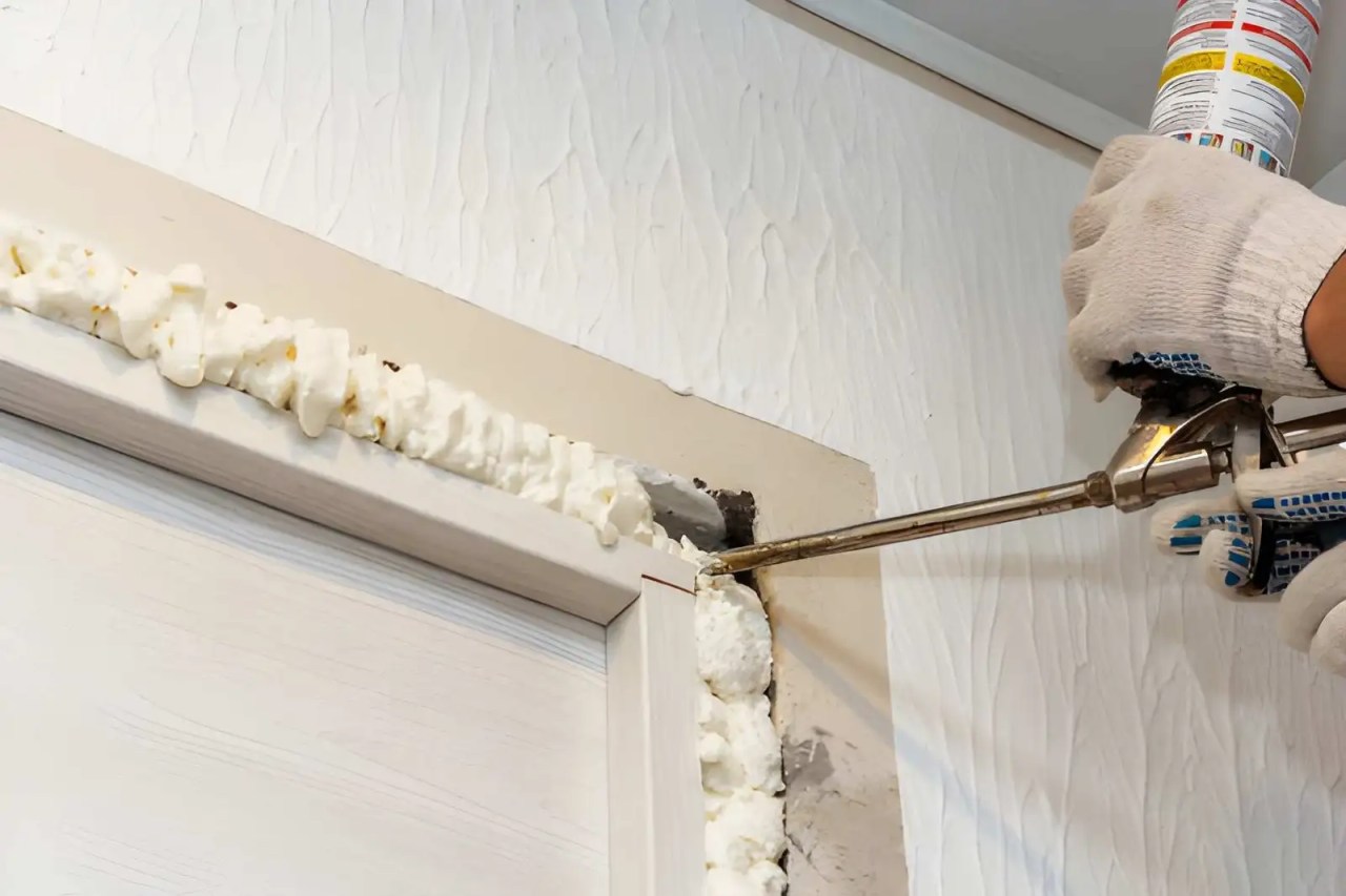 technician applying expanding foam insulation around an exterior door frame during exterior door installation.