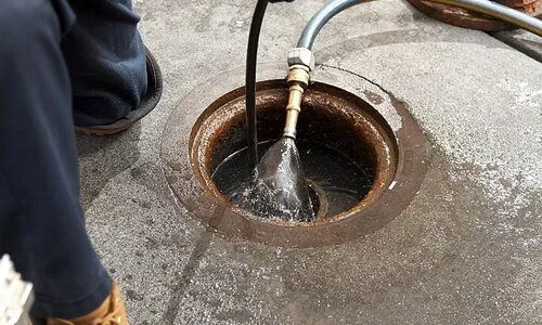 technician using a hose to pump water out of a sump pump pit in a basement floor.