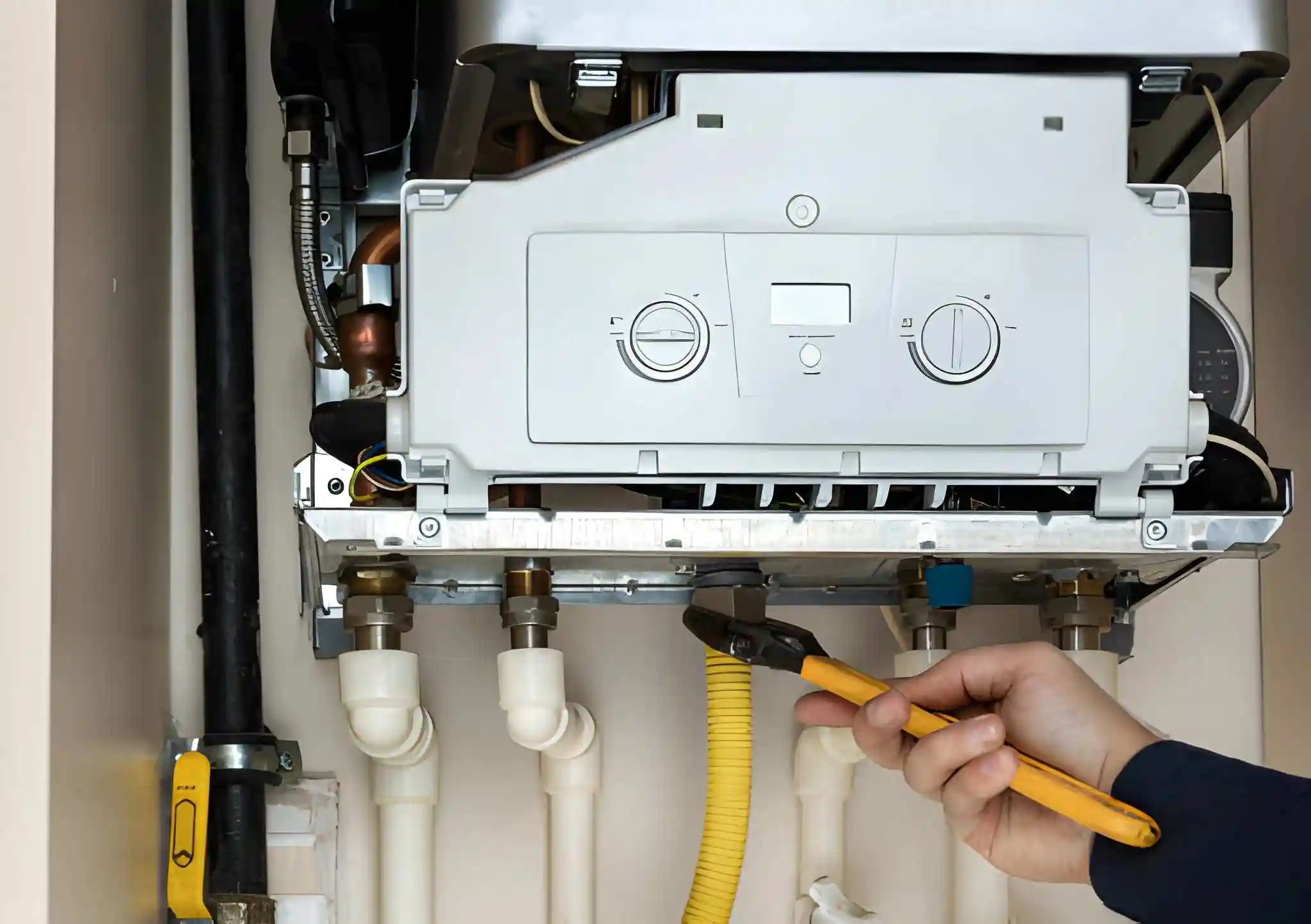 technician holding a tool while inspecting the underside of an open furnace or boiler unit with visible pipes and gas line connections. furnace installation in centreville va