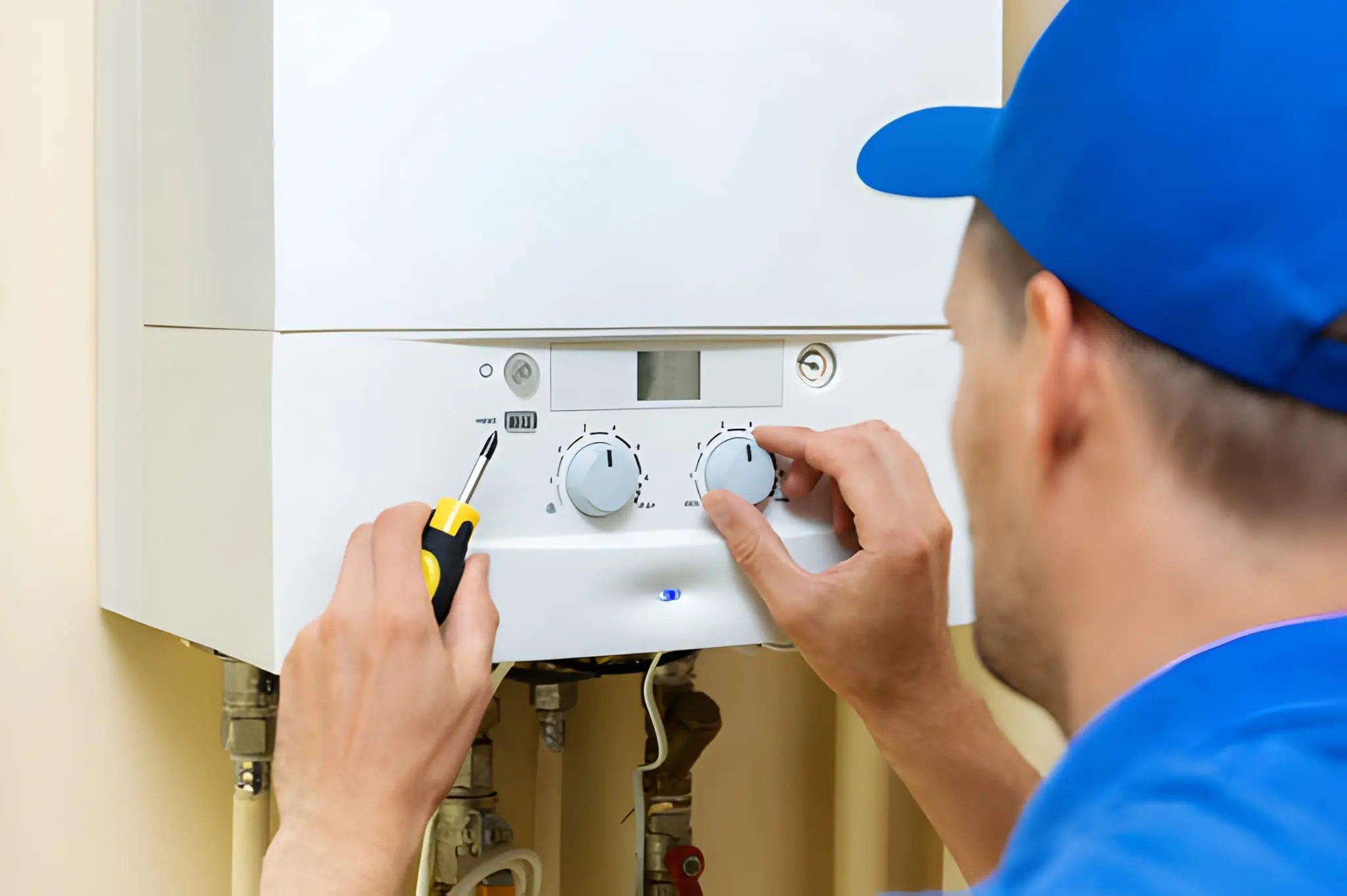 technician in a blue uniform adjusting the control knobs on a wall-mounted furnace or boiler while holding a screwdriver. furnace installation in falls church va