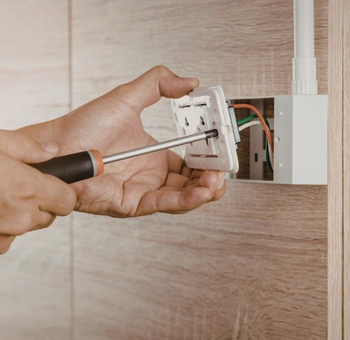 a close-up of a technician's hands using a screwdriver to secure a white faceplate during a professional gfci outlet repair in burke va.
