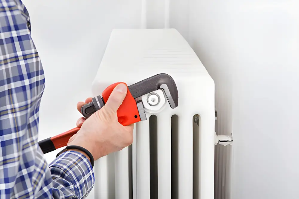 technician using a wrench to repair a white residential radiator heater. heating repair in falls church va