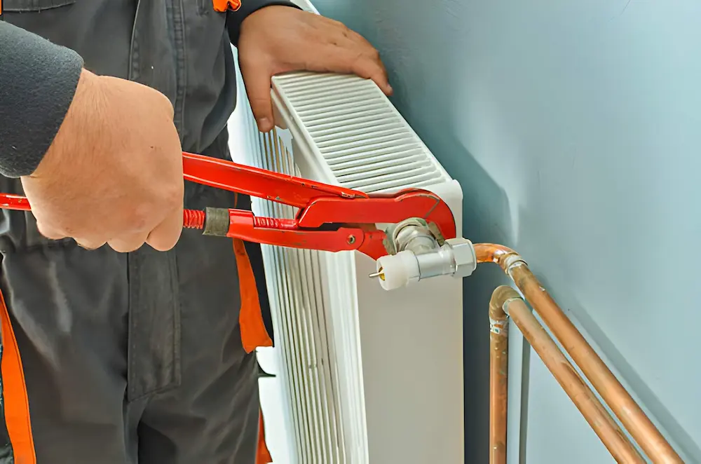 technician using a large red pipe wrench to tighten a radiator valve connection during heating repair in merrifield va.