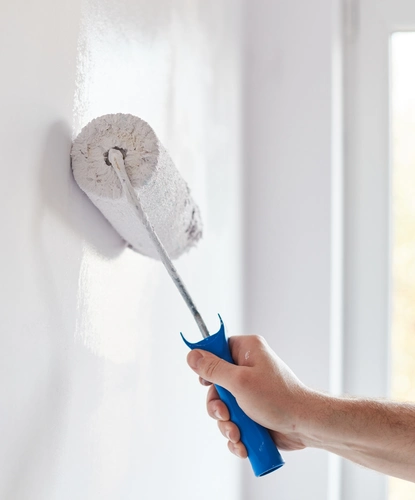 hand using a paint roller to apply white paint on an interior wall during professional painting service.