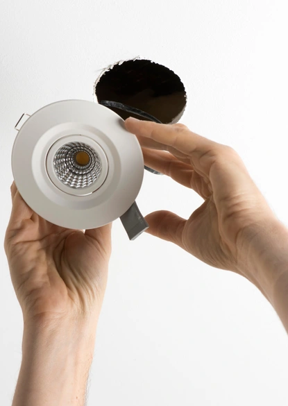 close-up of a technician's hands carefully installing a white recessed ceiling fixture during an led lights replacement in herndon va.