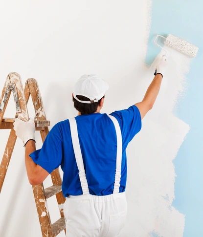 professional painter using a roller to apply blue paint to an interior wall next to a ladder.