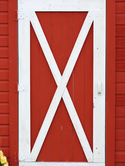 professional barn door installation and repair in centreville va showing a red wooden barn door with a white x-brace design and white hinges.
