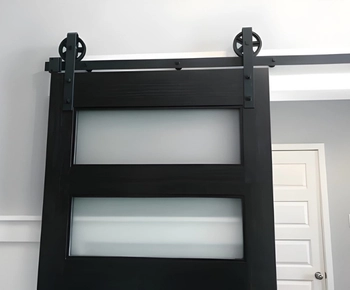 professional barn door installation in fairfax va showing a modern black wooden sliding door with frosted glass panels and black hardware.